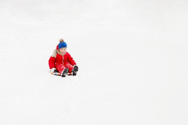 El niño se desliza sobre una tabla en la nieve blanca.
