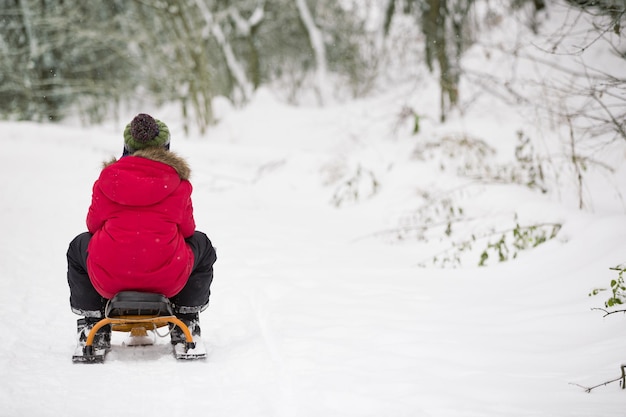 Niño deslizándose por la colina en el bosque de invierno y divirtiéndose con la nieve. concepto de estilo de vida