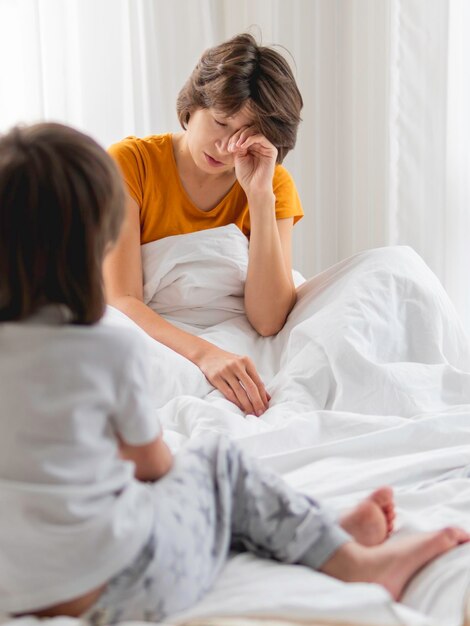 Foto el niño despierta a su madre somnolienta desordenada madre se sienta en la cama incómoda vida como padre