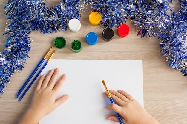 Un niño dibuja un árbol de Navidad Ideas para dibujar con colores brillantes Dibujar niños sobre un fondo blanco Una niña pequeña dibuja con pintura y pinceles El concepto de desarrollo infantil