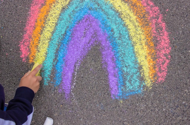 Un niño dibuja un arco iris sobre el asfalto Enfoque selectivo