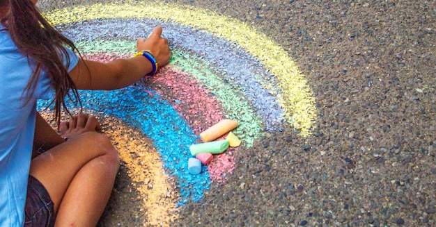 Un niño dibuja un arco iris sobre el asfalto Enfoque selectivo