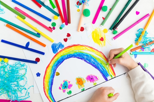 Foto niño dibuja un arcoiris con marcadores