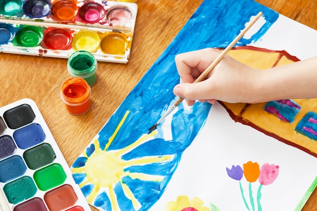 Foto un niño dibuja la casa y las flores con pintura. enfoque selectivo