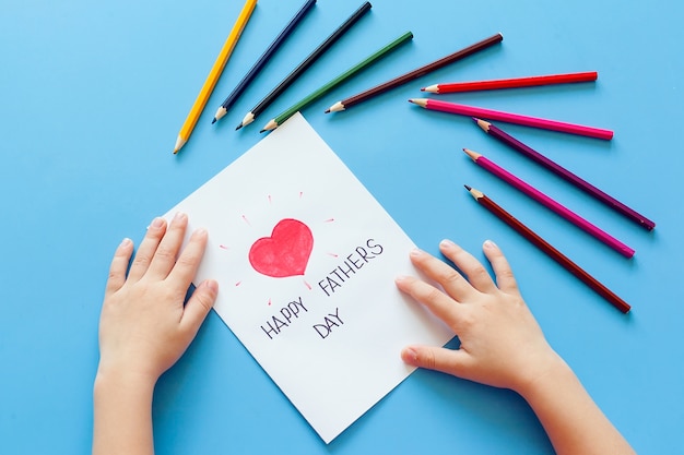 Un niño dibuja una tarjeta con lápices para el día del padre.