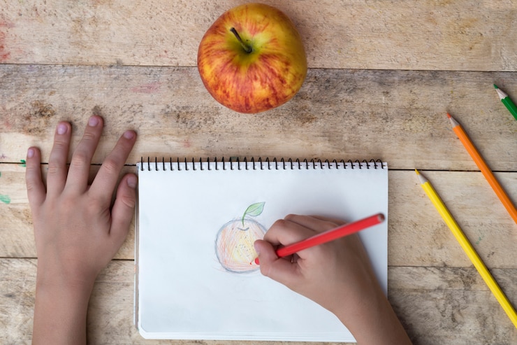 Foto niño dibujando una manzana con lápices de colores