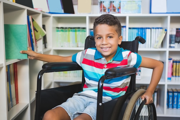 Niño discapacitado seleccionando un libro de estantería en la biblioteca