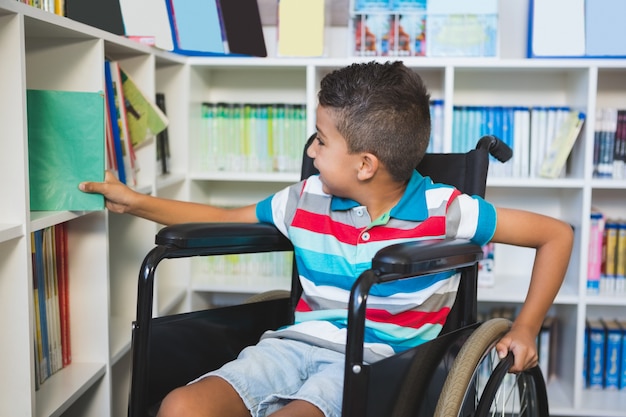 Niño discapacitado seleccionando un libro de estantería en la biblioteca