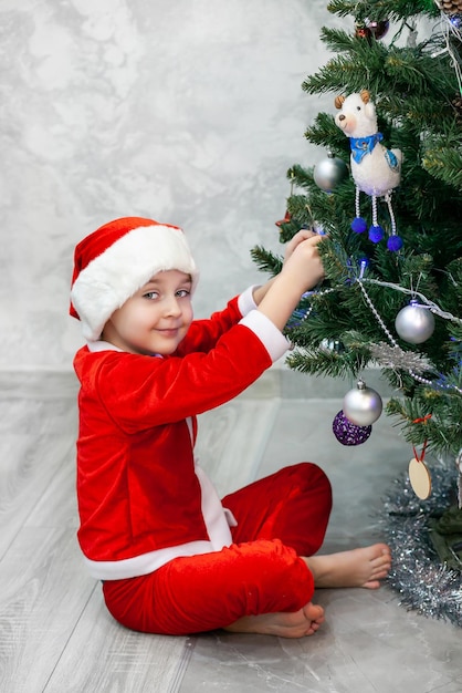 Un niño disfrazado de Papá Noel está decorando un árbol de Navidad