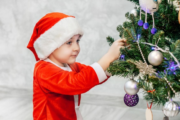 Un niño disfrazado de Papá Noel está decorando un árbol de Navidad