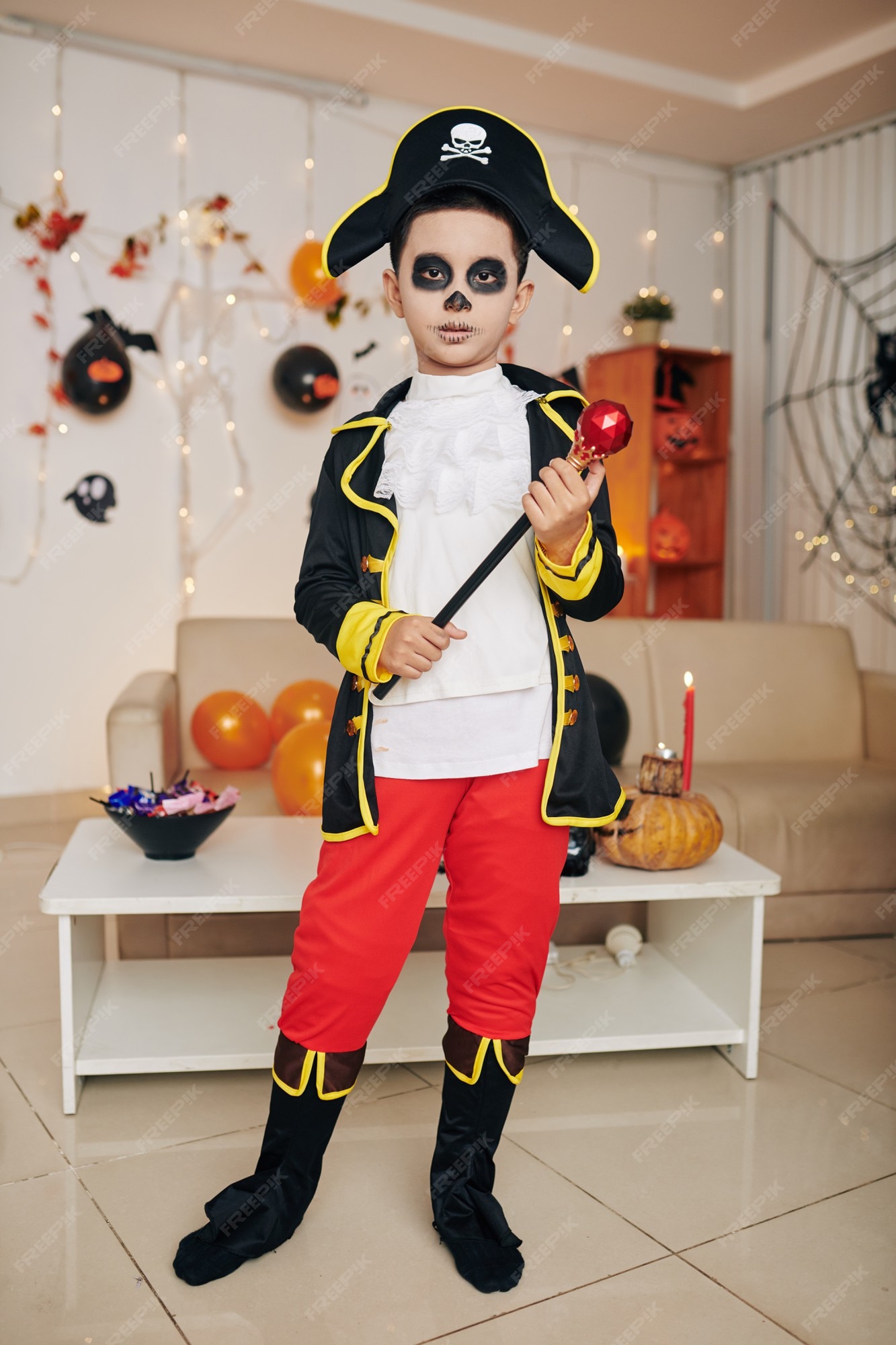 sol Marinero suerte Niño disfrazado de pirata de halloween sosteniendo el cetro cuando está de  pie en la habitación decorada para la fiesta de halloween | Foto Premium