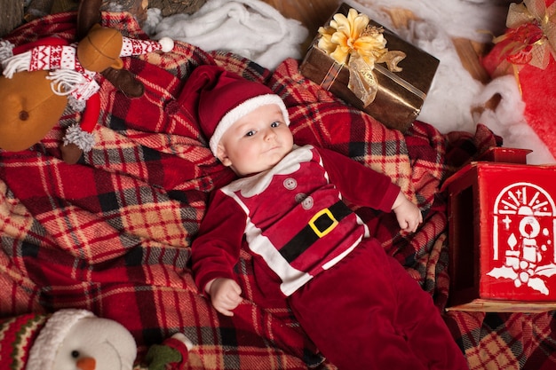 Un niño disfrazado de Santa Claus descansa sobre un plaid rojo rodeado de juguetes