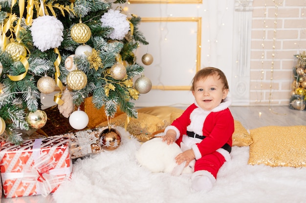 Un niño disfrazado de Santa se sienta en el árbol de Navidad con un conejo, el concepto de año nuevo y Navidad