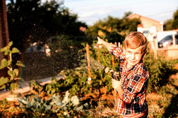 El niño disfruta de un arcoíris mientras riega el jardín.