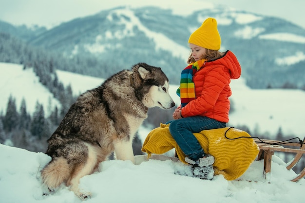 Niño disfruta de un paseo en trineo con un perro husky siberiano trineo infantil montando un trineo los niños juegan en la nieve