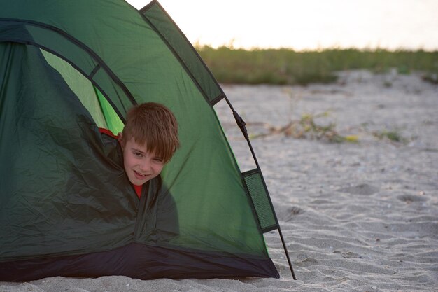 Niño disgustado asomándose de la carpa turística Temprano en la mañana Vacaciones de verano y viaje