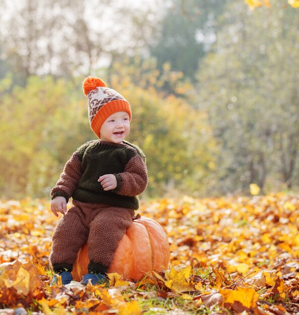 Niño divertido con calabaza naranja en el parque otoño