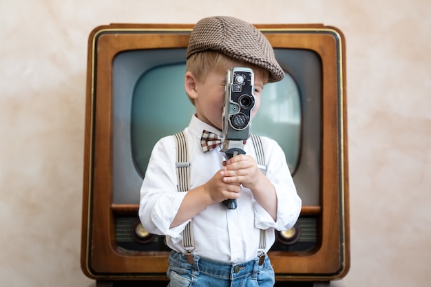 Niño divertido con cámara vintage. Niño feliz divirtiéndose en casa. Concepto de cine retro