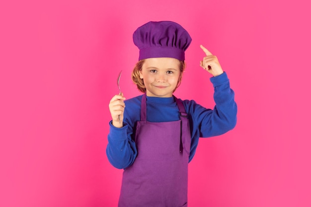 Niño divertido chef cocinero con cuchara Niño en uniforme de cocina y sombrero de chef preparando comida sobre fondo de color de estudio Cocina culinaria y concepto de comida para niños