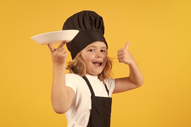 Niño divertido cocinando con un plato de cocina Niño chef cocinando prepara comida en un estudio aislado Niños cocinando Niño adolescente con delantal y sombrero de chef preparando una comida saludable