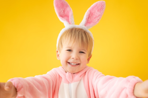 Niño divertido con conejito de Pascua contra la pared amarilla.