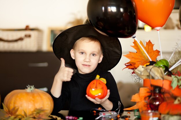 Niño divertido disfrazado de bruja para Halloween con calabaza Jack en manos.