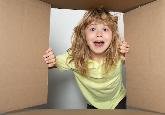 Niño divertido y emocionado de 9 años de edad desempacando y abriendo la caja de cartón mirando dentro Los niños pequeños desempaquetando el regalo dentro de la vista Servicio de entrega de paquetes