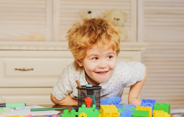 Niño divertido juega en el constructor en la sala de juegos niños cara divertida Niños jugando con bloques de colores retrato de cabeza