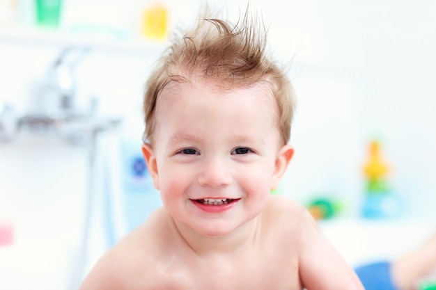 Niño divertido jugando con agua y espuma en un baño