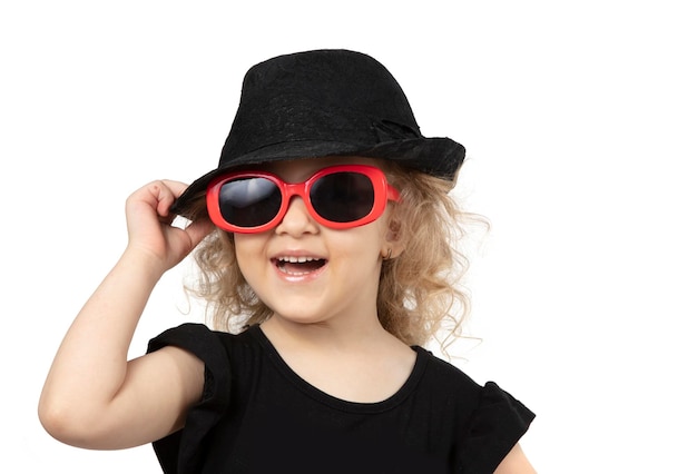 Niño divertido Niña pequeña con un sombrero negro y gafas de sol sobre un fondo blanco