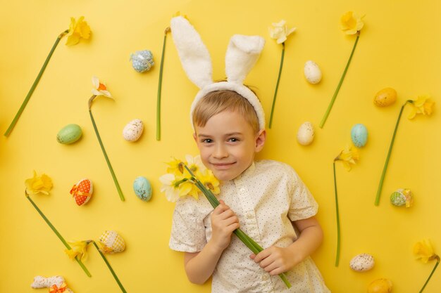 Niño divertido niño feliz con huevos de pascua y flores de primavera sobre fondo amarillo