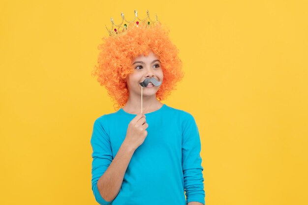 Niño divertido de nuevo estilo con bigote de fiesta, niña adolescente egoísta en el concurso de tiara, día de los inocentes, simplemente divirtiéndose, fiesta elegante, mirada egocéntrica, niño con peluca de payaso y corona, imagínese princesa