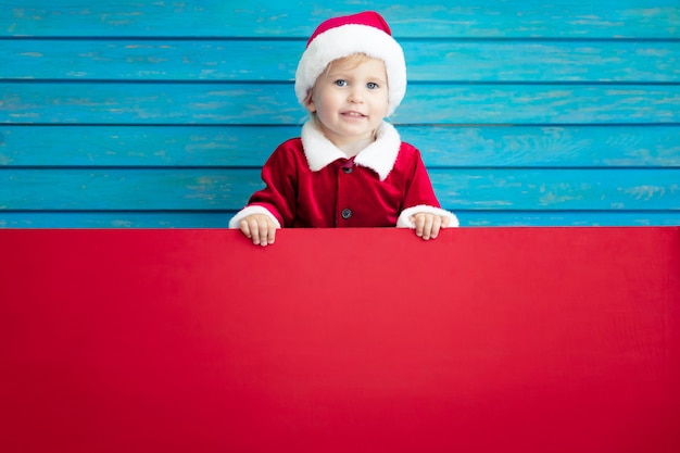 Niño divertido con pancarta de cartón en blanco. Niño jugando en casa. Concepto de vacaciones de Navidad. Copie el espacio.