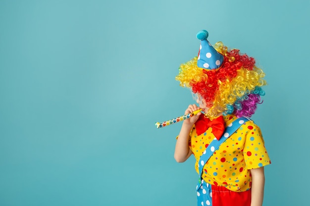 Niño divertido payaso contra fondo azul Niño feliz jugando con decoración festiva 1 día de los inocentes