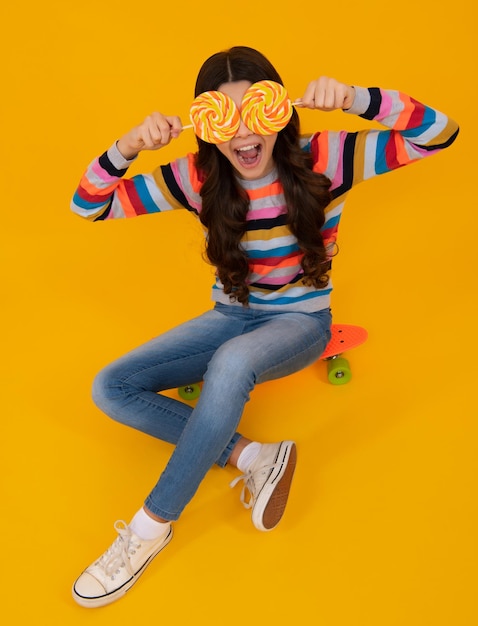 Niño divertido con piruleta sobre fondo amarillo aislado Dulce infancia vida Chica adolescente con delicioso caramelo piruleta tienda de dulces Adolescente feliz emociones positivas y sonrientes de chica adolescente