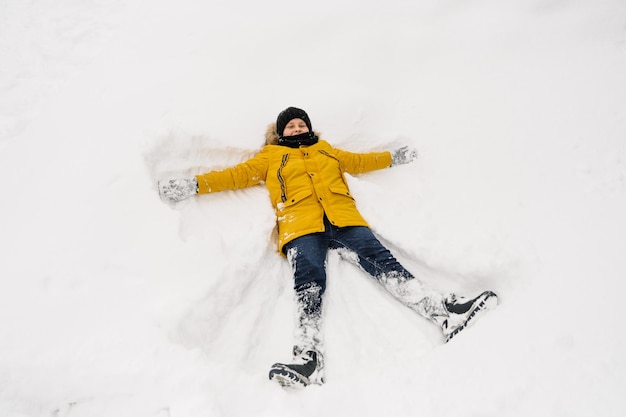 Niño divertido en ropa de invierno amarillo camina durante una nevada. Actividades de invierno al aire libre para niños Vacaciones familiares de invierno con niños