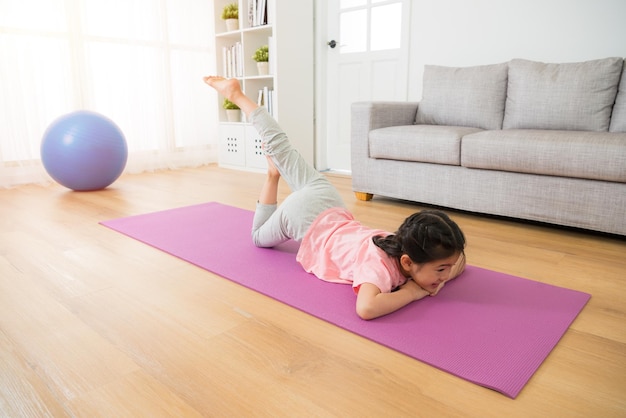 un niño divirtiéndose haciendo gimnasia matutina con ejercicios de estiramiento en casa acostados en el suelo con alfombra en la sala de estar. actividad familiar y concepto de estilo de vida saludable.