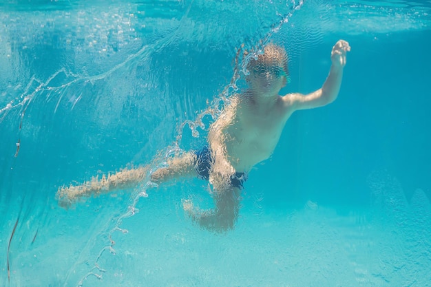 Niño divirtiéndose jugando bajo el agua en la piscina en vacaciones de verano