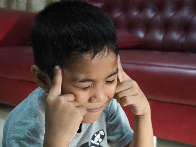 Un niño con dolor de cabeza En el fondo del sofá rojo de la casa.