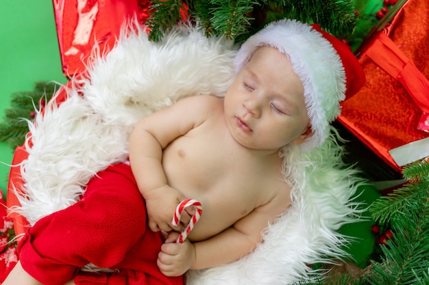 Un niño dormido en un traje de Papá Noel yace con un caramelo en sus manos sobre un verde