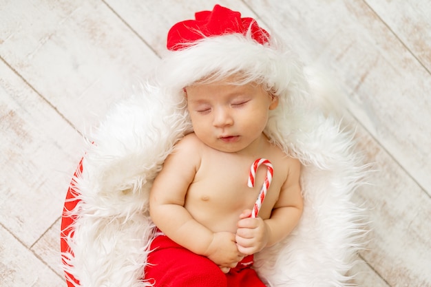 Un niño dormido en un traje de Santa se encuentra con un caramelo en sus manos sobre un fondo de madera clara