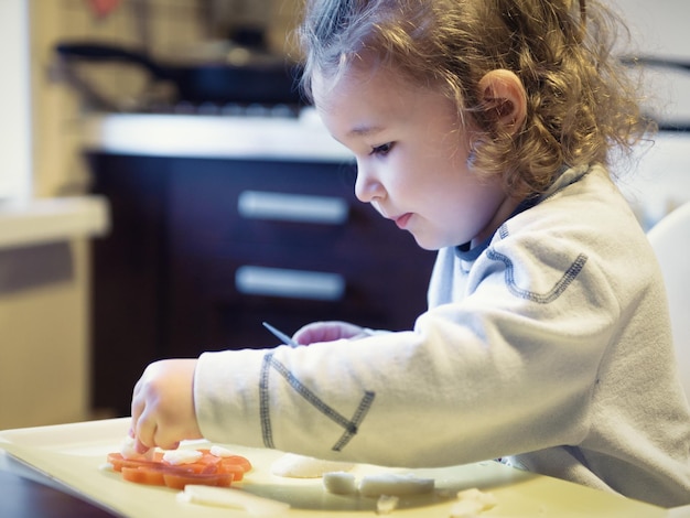 Niño de dos años corta zanahorias y papas en la cocina