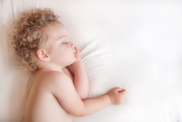 Niño de dos años durmiendo en una cama blanca