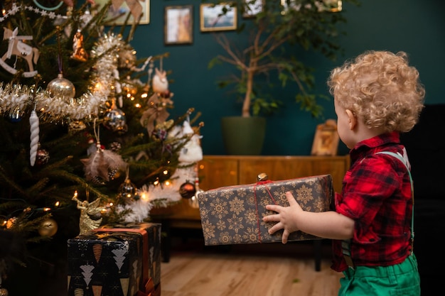 Un niño de dos años lleva un paquete de regalos el día de Navidad