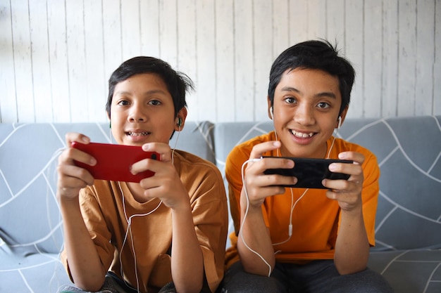 Niño de dos jugadores sonriendo a la cámara mientras juega juegos en el teléfono inteligente Niños modernos o milenarios adictos