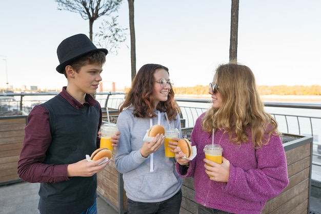 Niño y dos niñas en la calle de la ciudad con hamburguesas y jugo de naranja