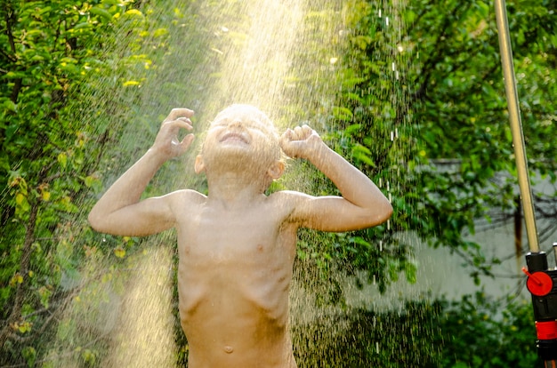 El niño bajo la ducha en el jardín.