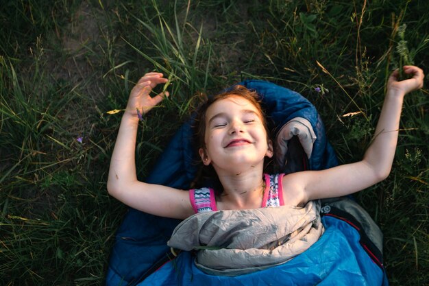 Un niño duerme en un saco de dormir sobre la hierba en un viaje de campamento Recreación ecológica al aire libre Estilo de vida saludable Horario de verano Sueño dulce y tranquilo Repelente de picaduras de mosquitos