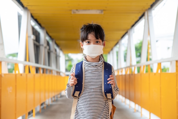 Niño en edad escolar con mascarilla durante el brote de coronavirus Niña que regresa a la escuela