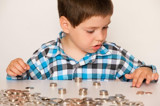 Un niño en edad preescolar con una camisa a cuadros cuenta monedas construye torres Educación financiera para niños